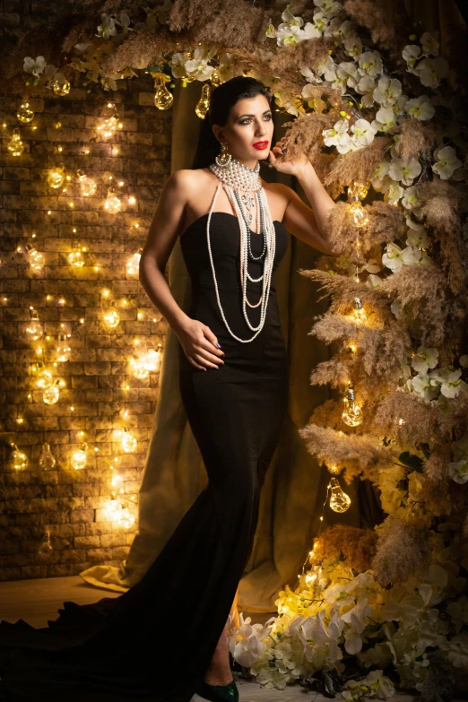 a woman in a black dress is posing in front of a backdrop with flowers