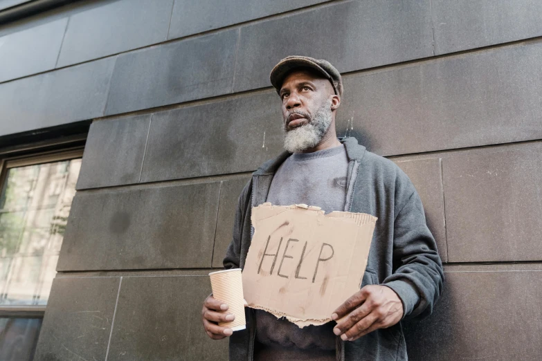 a man holding a coffee cup and paper sign that reads help