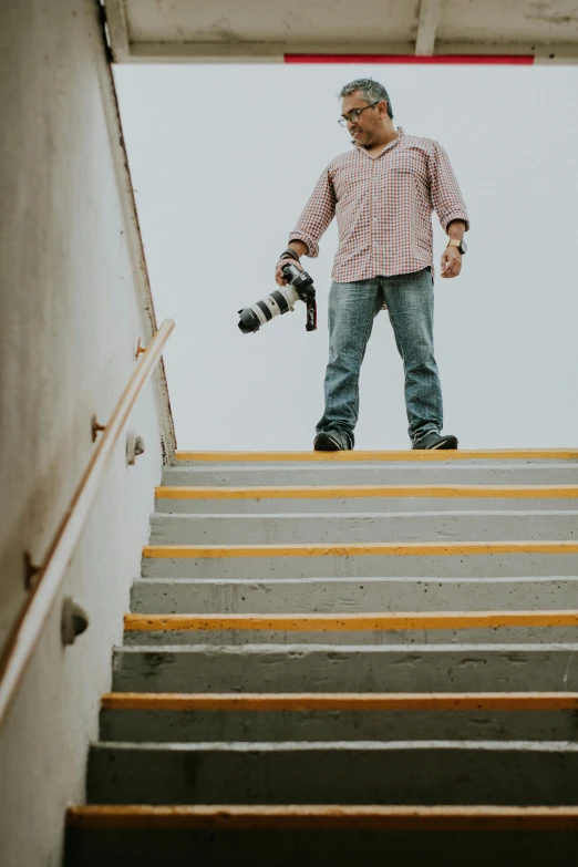 an older man holding two cameras as he stands on the steps of stairs