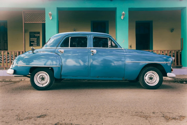 an old blue car is sitting in front of a building