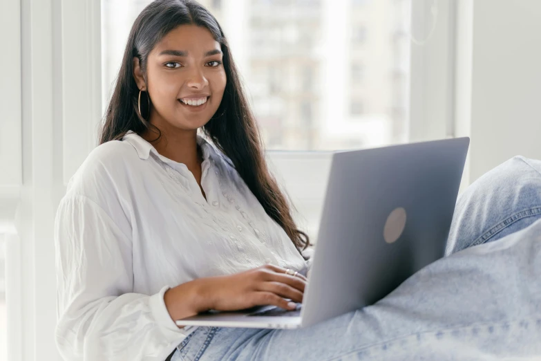 woman on laptop sitting on bed smiling with white walls