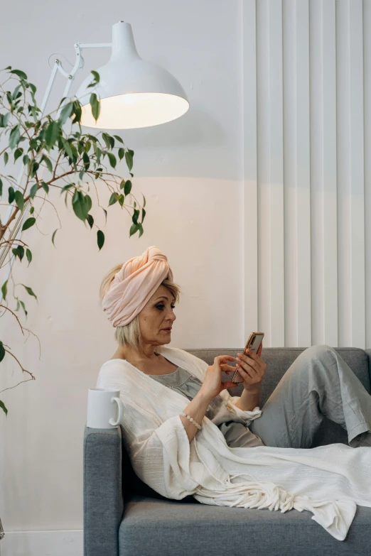 a woman is sitting on the couch while she is holding a cellphone