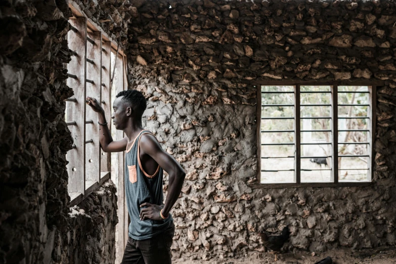 a black man stands in an empty room with rocks on the wall