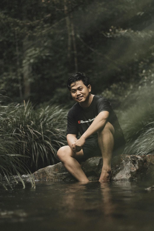 young man in black shirt sitting on rock and looking away from camera