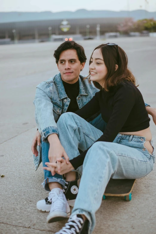 a young woman sitting next to a man who is sitting on top of a skateboard