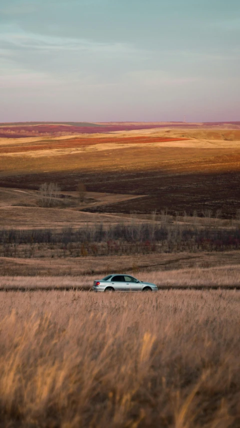 a car driving through a field in front of mountains