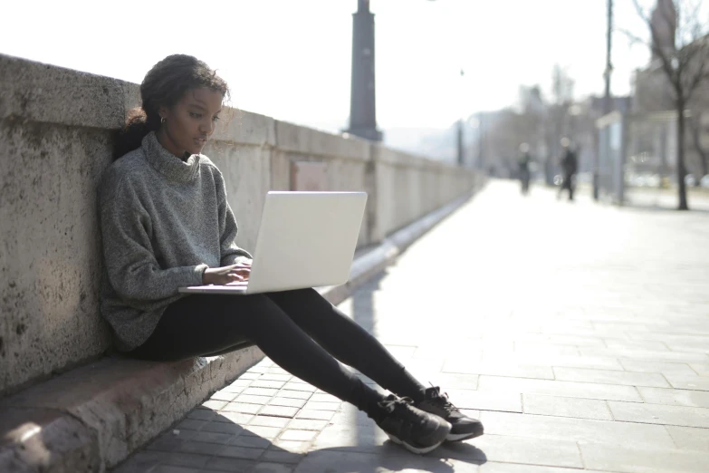 a woman sitting on the side of a building with her laptop