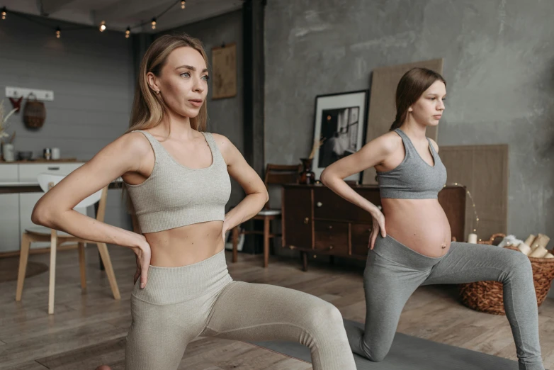 two women in grey and white outfits standing on a yoga mat, in a studio