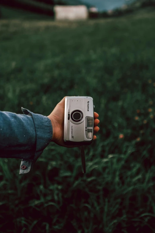 a hand holding a small camera in the middle of the grass