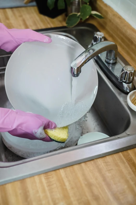 a person in pink gloves and pink rubber gloves washes dishes