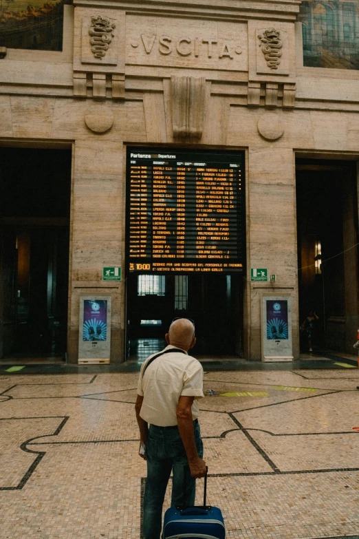 a man holding a suitcase in front of a el with a departure screen