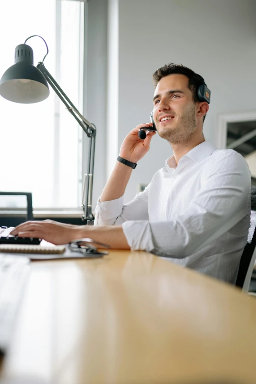 a man in headphones talking on a phone next to a computer