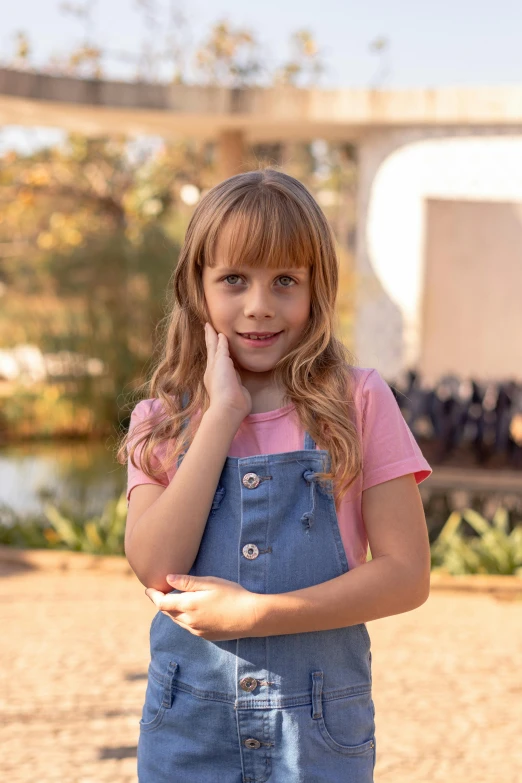 a girl in a denim dress with her chin resting on her hand