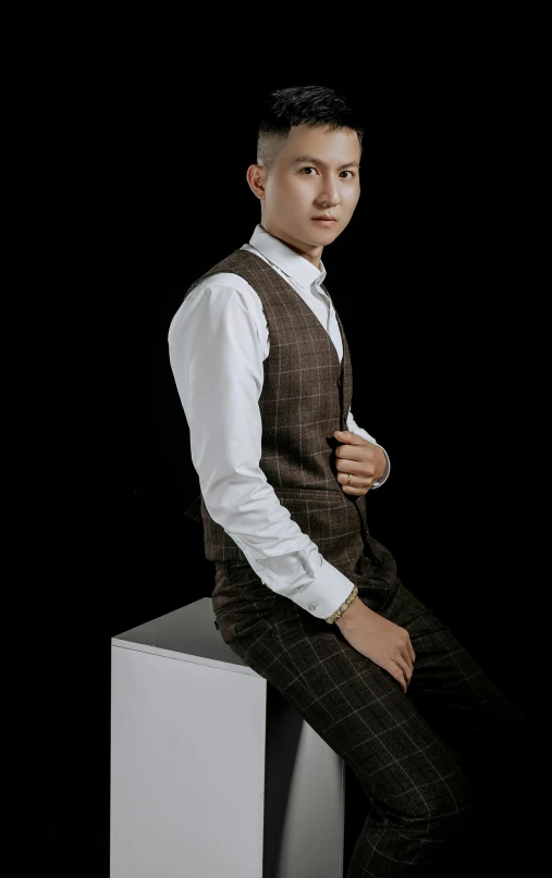 a man in a dress vest and white shirt is sitting on a stool