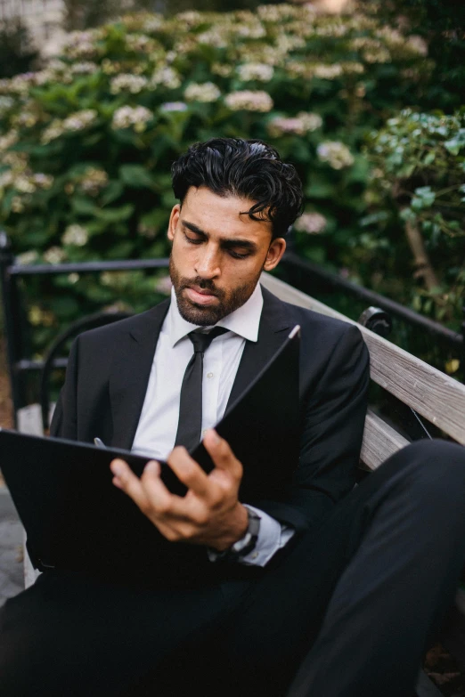 a man in a suit is sitting on a bench with an ipad