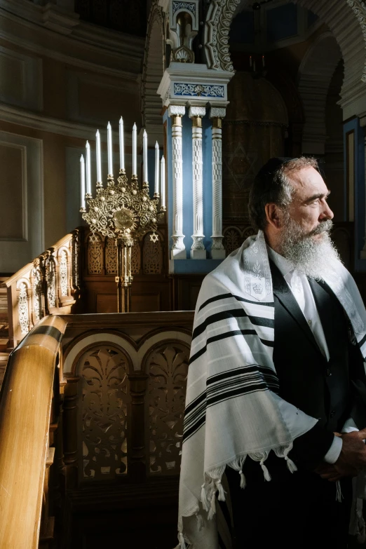 a man with a white and black robe standing by some candles