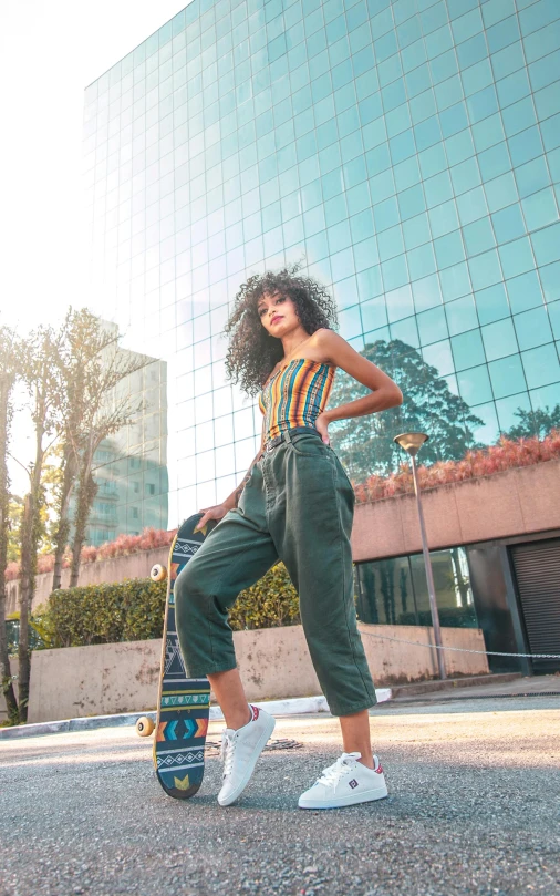 a woman holding her skateboard and posing in front of a building