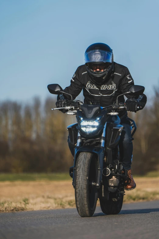 a man on a motorcycle with its helmet and glove on riding down the road