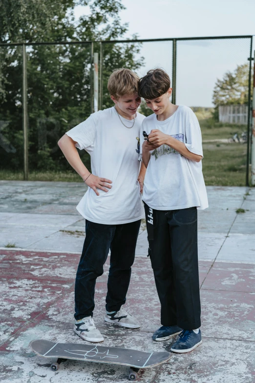 two guys standing near each other, one on a skateboard