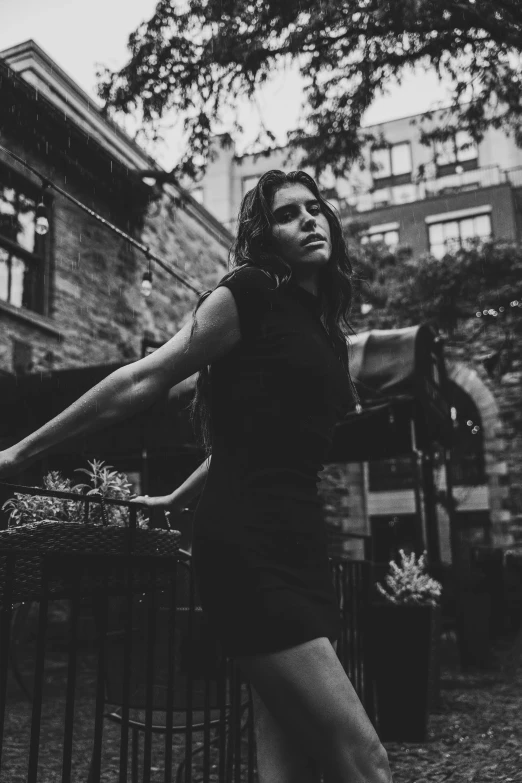 black and white image of woman leaning on fence in urban setting