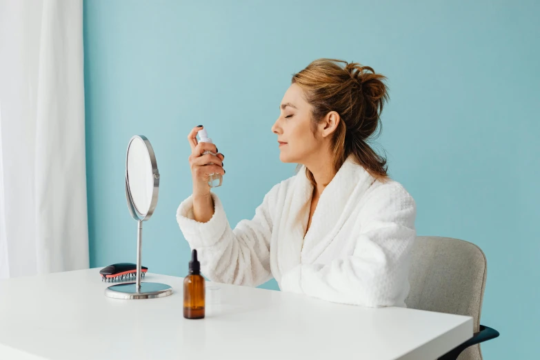 a woman in white robe holding up her lipstick in front of a mirror