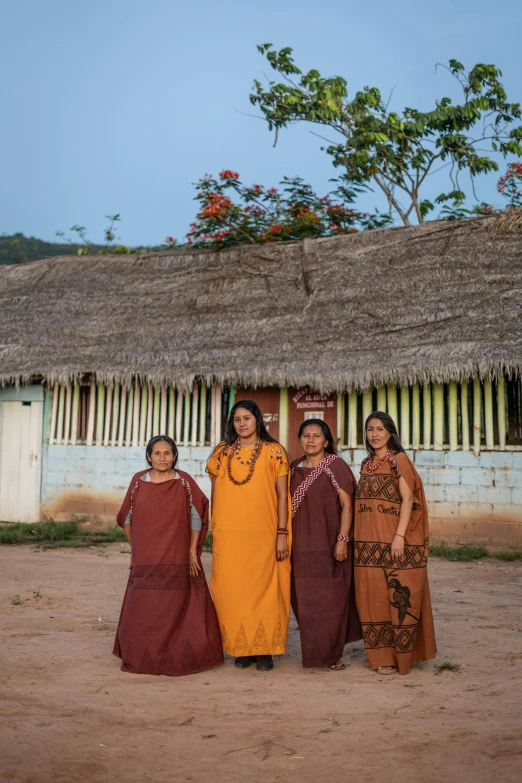 three indian ladies are standing beside a hut