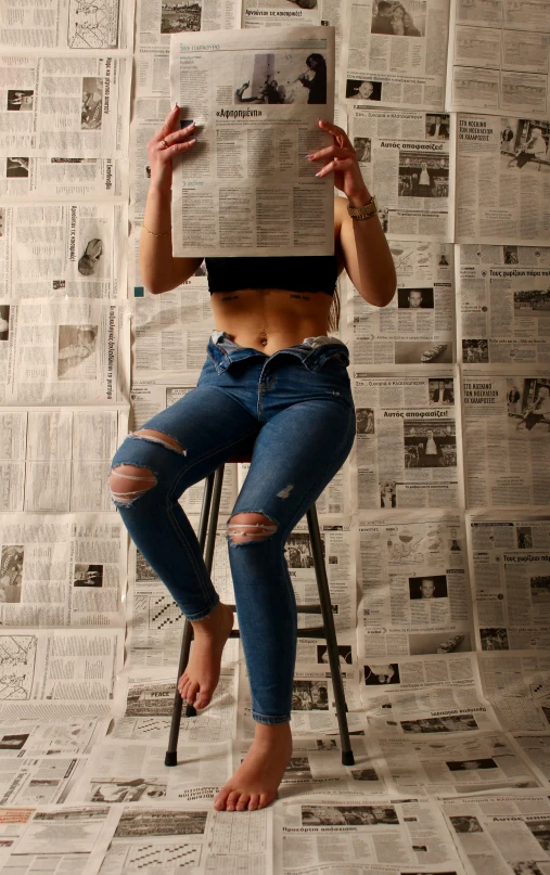 woman with ripped jeans sits on chair reading newspaper