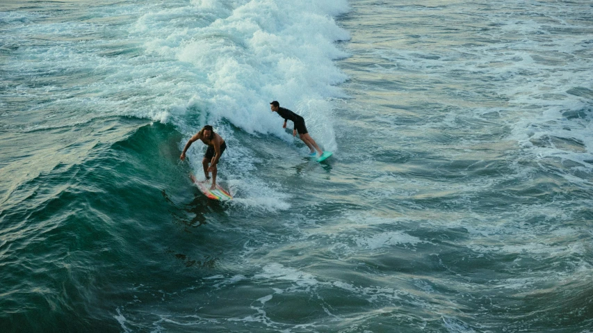 two people on surfboards ride on top of waves