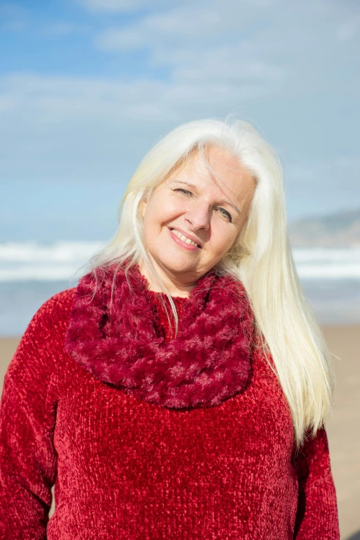 a smiling woman in a red sweater and matching fur poses by the beach