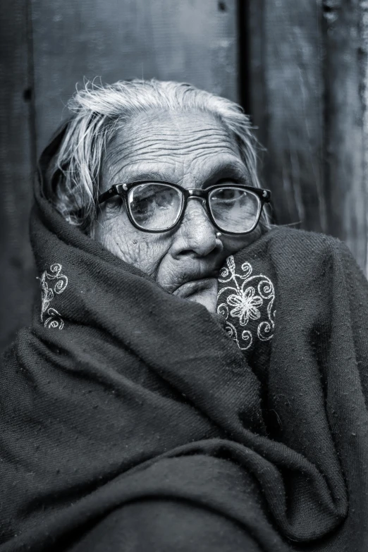 an old woman has glasses and has a black blanket