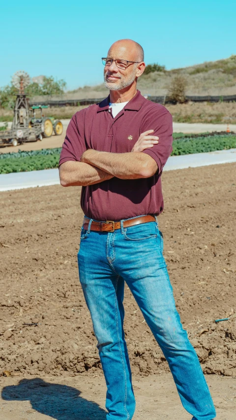 a man standing with his arms crossed on top of a dirt field