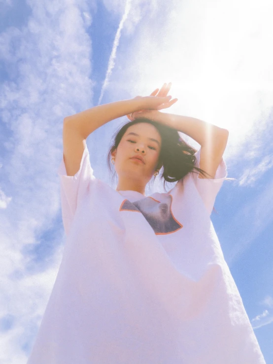 woman with arms raised standing under cloudy blue sky