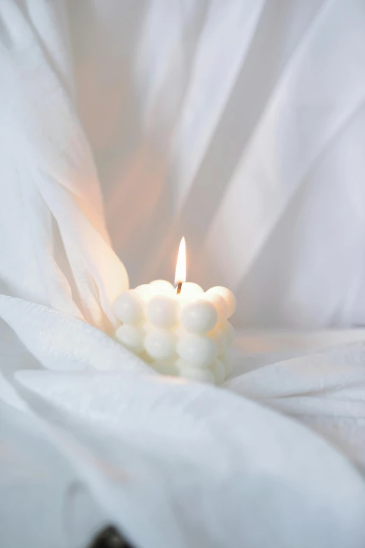 a white candle burning in an untuttoned curtain