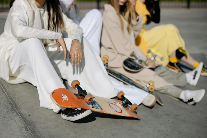 three girls wearing white long sleeve dresses sitting and one girl with orange skateboard in background