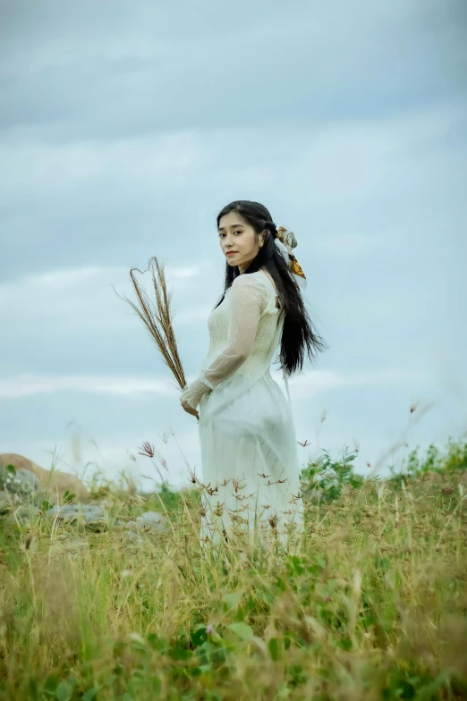 woman wearing white dress holding sticks standing in grass