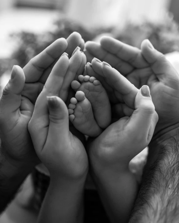 this black and white po shows many hands holding a newborn baby's feet