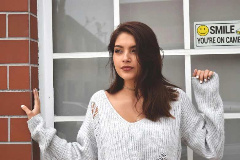 a young woman wearing a white sweater holds a sign