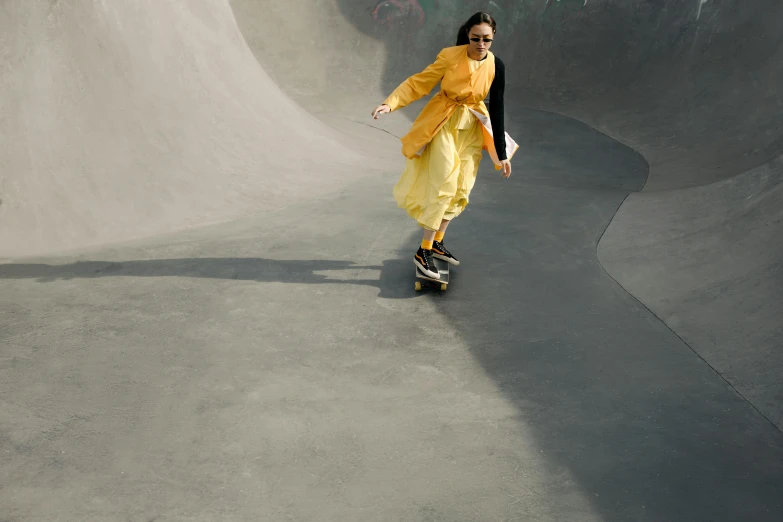 a girl skateboarding down a concrete ramp wearing an orange dress