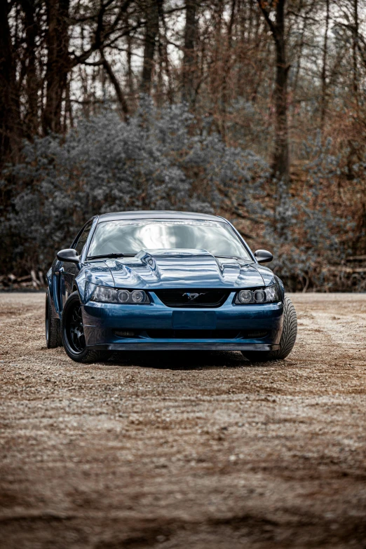 a blue sport car in the sand with trees in the background