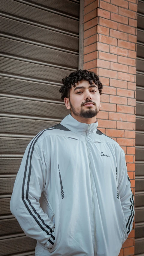 a man with curly hair standing near a brick building