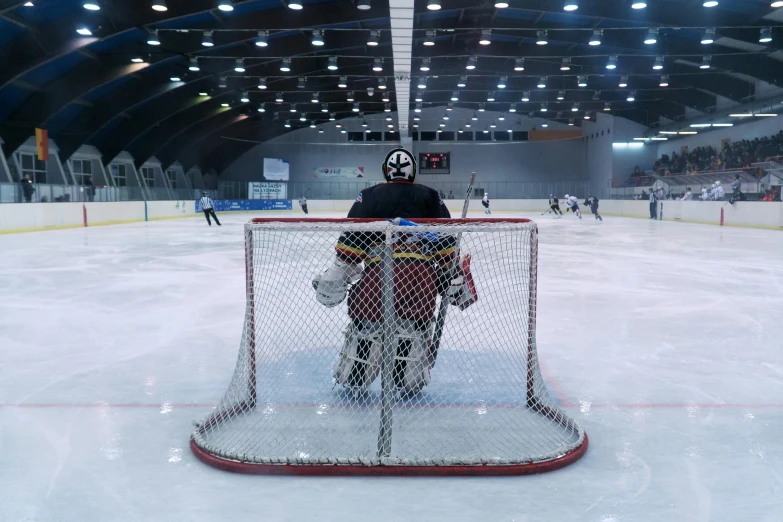 the goalie in a black jacket is behind a goal net