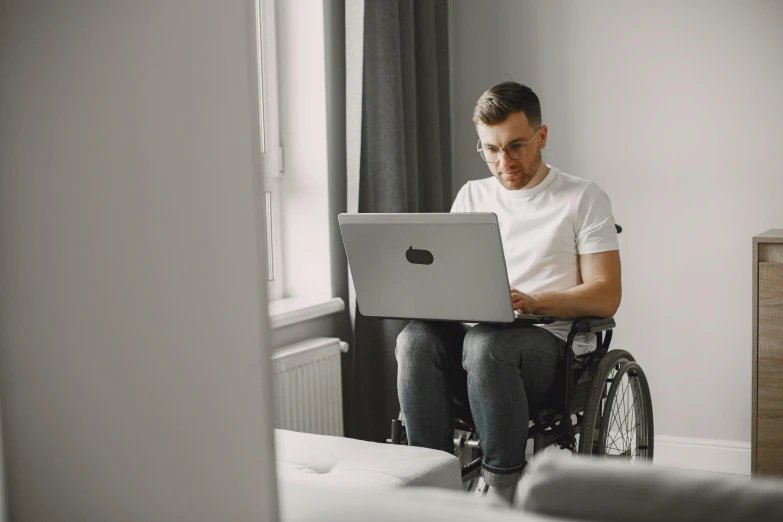 the man sits in a wheel chair and uses his laptop