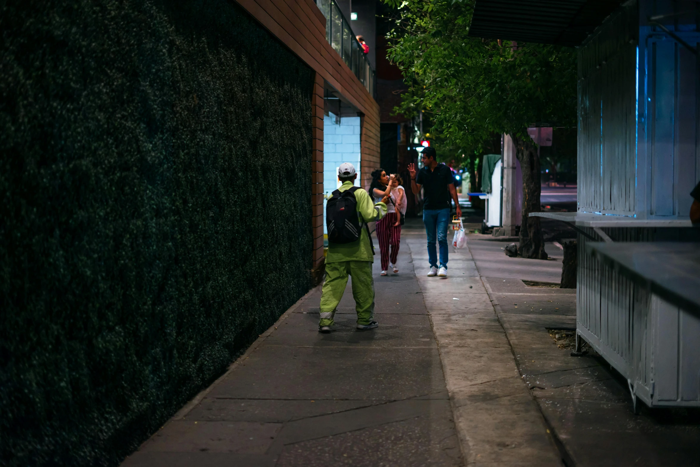 a man in green walks down the sidewalk of a sidewalk shopping area