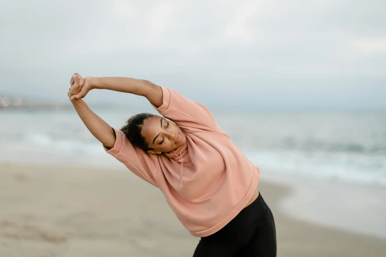 an asian woman stretches on a beach near the ocean