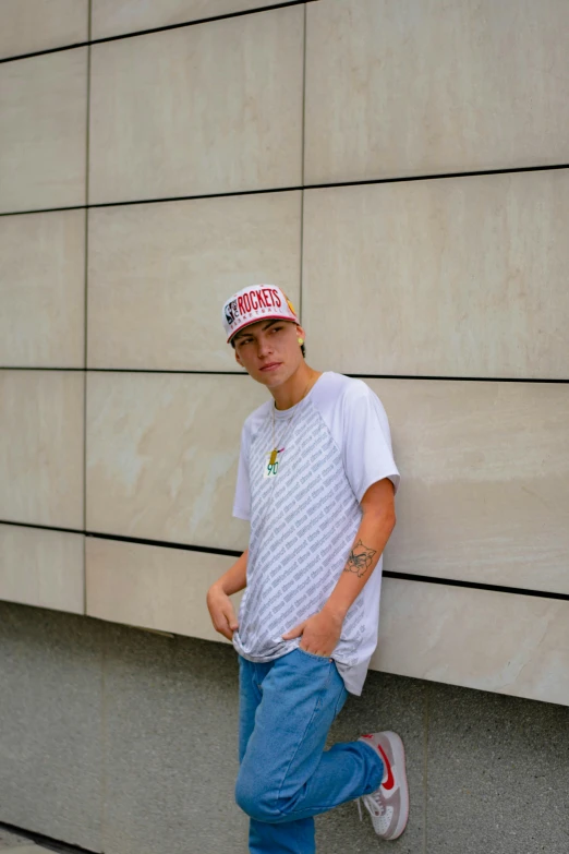 a boy standing by the wall wearing a hat