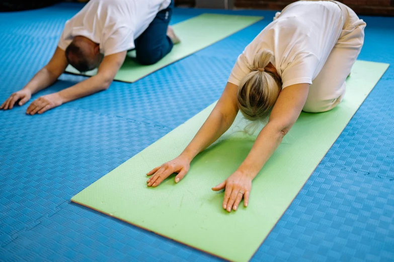 two people practicing yoga on blue mats in a gym