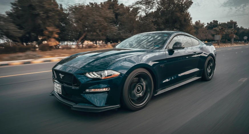 blue ford mustang with black wheels driving down the street