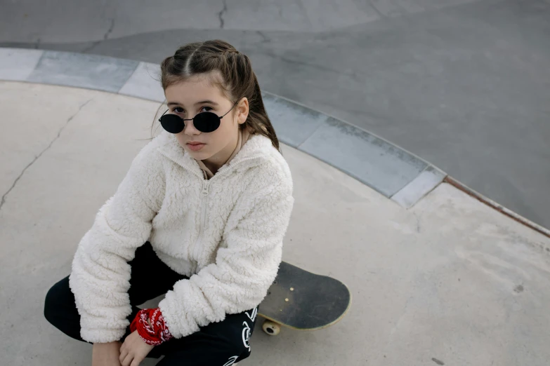 a woman in sunglasses and a white sweater sitting on top of a skateboard