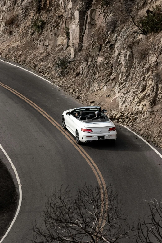 a white convertible car driving down a winding road