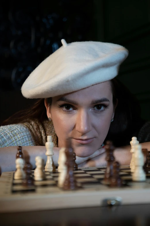 woman with beret playing chess while sitting behind a table